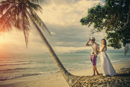 happy newlyweds of steam stand on the beach, against the background of the sea and palm treesの写真素材