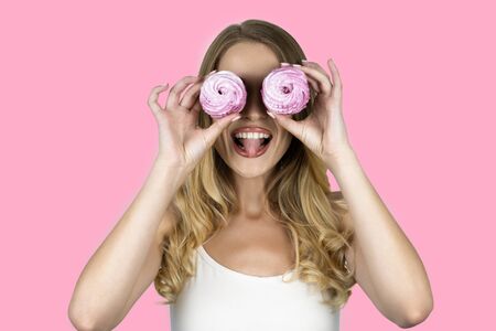 Girl with cupcakes near eyes looks happy isolated pink backgroundの写真素材