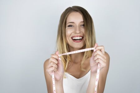 young attractive blond woman looks happy holding centimeter in her hands white isolated background
