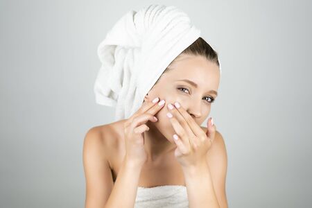 beautiful woman in white towel on her head squeezing pimple on her cheek isolated white backgroundの写真素材