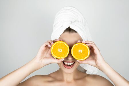 funny young smiling woman in white towel on her head holding oranges near her face isolated white backgroundの写真素材