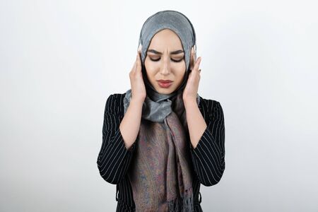 young beautiful irritated Muslim woman wearing turban hijab, headscarf looking angry with her hands closing ears isolated white backgroundの写真素材