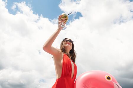 beautiful sexy young brunette woman with perfect body wearing red swimsuit holding cocktail on cute...