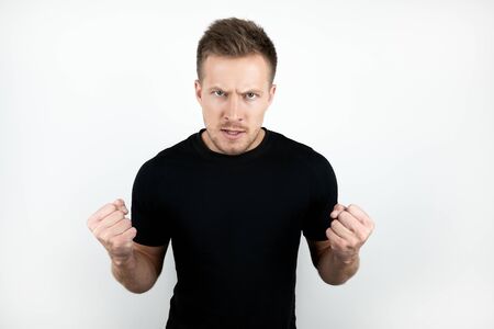 handsome young man wearing black t-shirt clenching his fists with anger isolated white backgroundの写真素材