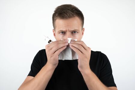 handsome young sick man blows his nose holding handkerchief on isolated white backgroundの写真素材
