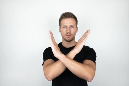 handsome young man wearing black t-shirt holding his arms crossed showing negative expression...
