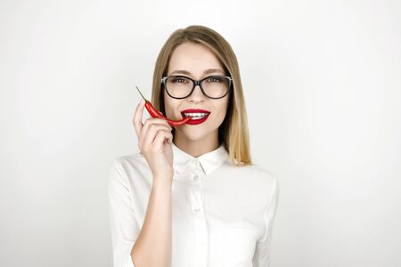 young beautiful blonde woman biting red chilly pepper isolated white backgroundの写真素材