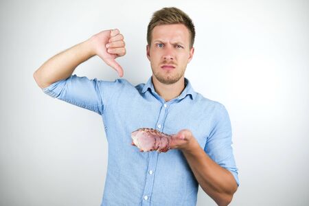 young handsome man holding sliced bacon showing dislike sign on isolated white background
