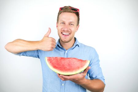 young handsome man with red eyeglasses on his head holding ripe watermelon showing like sign on isolated white backgroundの写真素材
