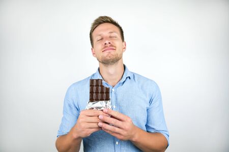 young handsome man holding chocolate bar looking pleased on isolated white background