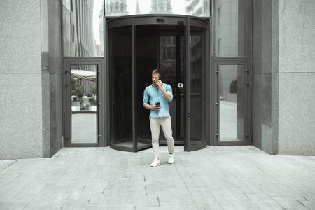 young handsome business man holding cup of coffee leaving office in the business center