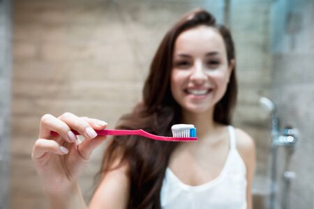 young beautiful smiling woman holds tooth brush with tooth paste in the bathroomの写真素材