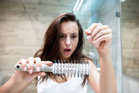 young beautiful surprised woman looking at her hairbrush full of hair lossの写真素材