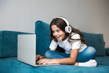 cute teenager girl in headphones lying on the sofa with laptop listening to musicの写真素材
