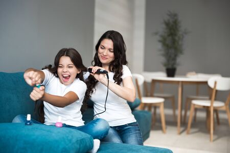 beautiful young mother with her cute teen daughter having beauty day applying nail polish and curling hair using curler both looking happyの写真素材