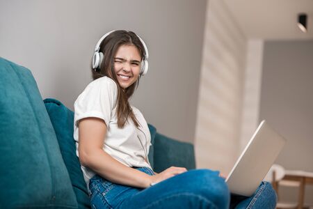 young beautiful woman in headphones working in her laptop on the sofa in the living room smilingの写真素材