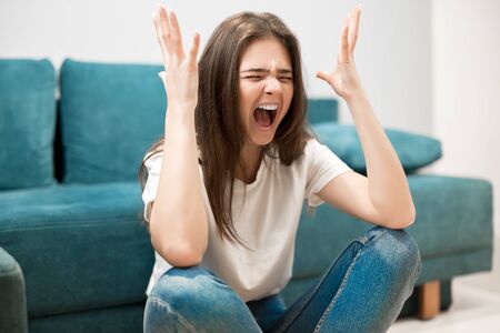 beautiful young woman crying feeling very depressed sitting on floor shouting loudの写真素材