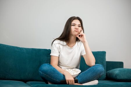 beautiful young woman cheers on her favorite team looking upset while watching football game eating popcorn on the sofa at homeの写真素材
