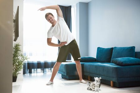 young handsome man doing sideways during warm up before workout at home looking satisfied sporty and healthy lifestyleの写真素材
