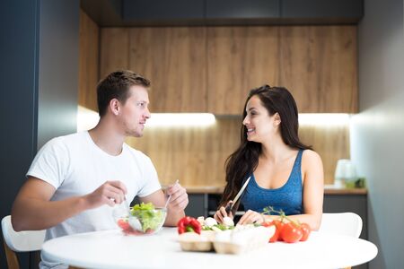 young couple handsome husband and his beautiful wife cooking breakfast in the kitchen together looking happy family traditionsの写真素材