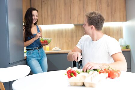 young couple cooking breakfast in the kitchen together husband chops cucumber helping to prepare salad his beloved wife family traditionsの写真素材