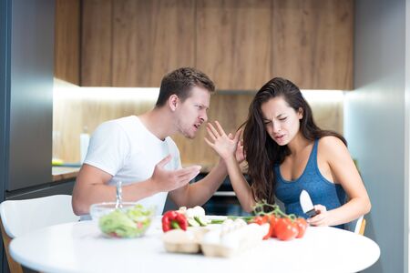 young couple having fight while cooking breakfast in the kitchen husband shouts loud at his wife family quarrelの写真素材