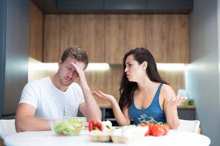young couple having fight while cooking breakfast in the kitchen husband looks tired and wife is irritated family quarrelの写真素材