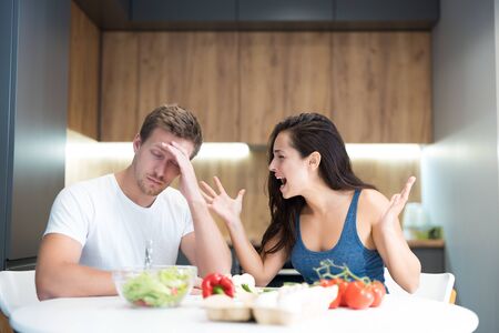 young couple having fight while cooking breakfast in the kitchen wife shouts loud at her husband while he looks annoyed family quarrelの写真素材