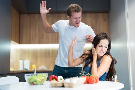 young couple having fight while cooking breakfast in the kitchen husband lifts his arm against his wife while she turns away family vilonceの写真素材