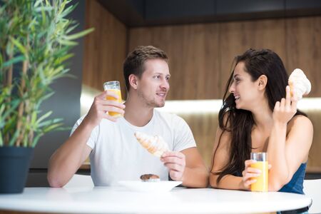 young lovely couple eating croissant and drinkink orange juice for breakfast in the kitchen start of great dayの写真素材