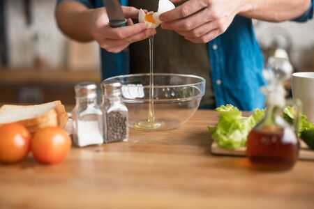 process of cracking egg into a glass plate by man with knife in his hand while preparing omelette for lunch.の写真素材
