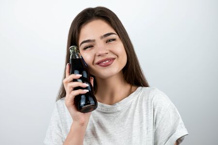 young attractive woman touching her face with bottle of soda drink with smile on her face on isolated white background dietology and nutritionの写真素材