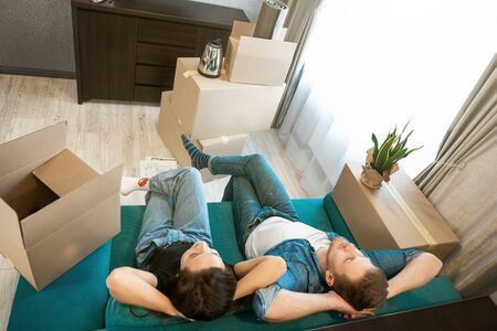 young couple man and woman looking tired having break on the sofa during moving to new appartment...