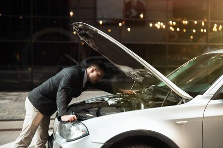 young handsome businessman standing near open front car bumper, checking engine , unexpectable vehicle trouble.の写真素材