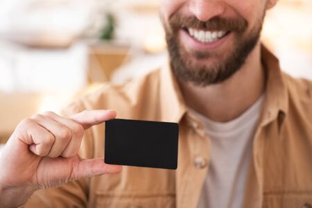 young man with beard holds bank card / business card smiling, close up.の写真素材