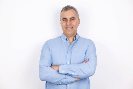 adult handsome man with grey hair wearing blue shirt standing in hand on hand pose on isolated white background, looks confidenの写真素材