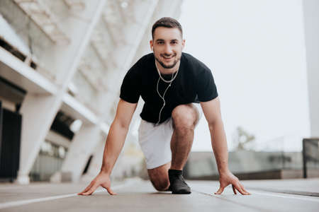 young smiling handsome brunette man in sportswear on ready position to run on the street stadium listens his favorite music, healthy fit lifestyleの写真素材