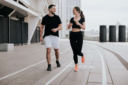 young couple handsome brunette man and beautiful woman in sportswear jogging on the street, everyday...