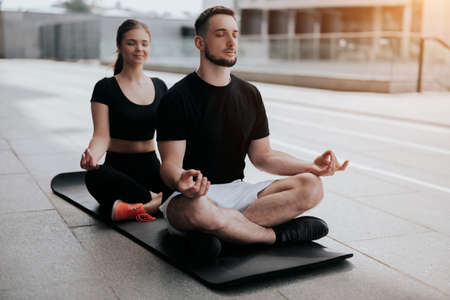 young couple handsome brunette man and beautiful woman in sportswear practicing yoga on mat on the street , relaxation , street workout, healthy fit lifestyleの写真素材