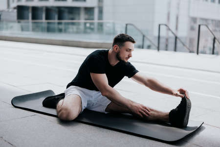 happy young handsome brunette man in sportswear warming up before street workout stretching on yoga mat, healthy fit lifestyleの写真素材