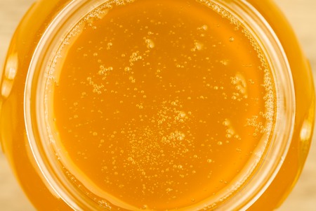 glass jar of fresh honey on wooden background, top view