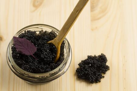 black Beluga caviar in glass jar on wooden background