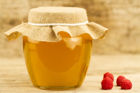 glass jar of honey closed jute cloth and raspberries on wooden backgroundの写真素材