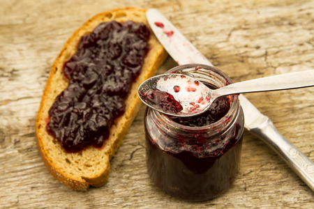 piece of rye bread with jam and knife on wooden backgroundの写真素材