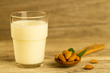 peeled almonds in a spoon c leaves and a glass of milk on wooden tableの写真素材