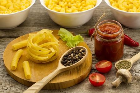 Ingredients for cooking pasta on wooden background. Chile pepper, cherry tomatoes, spices, mushrooms, tomato sauce. Healthy nutrition.の写真素材