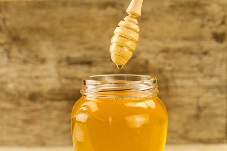 glass jar of honey with drizzler on wooden backgroundの写真素材