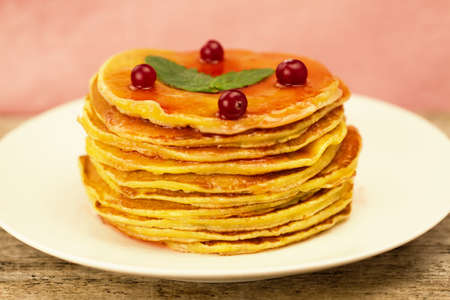 a stack of pancakes on a white plate with berries and jam on wooden backgroundの写真素材