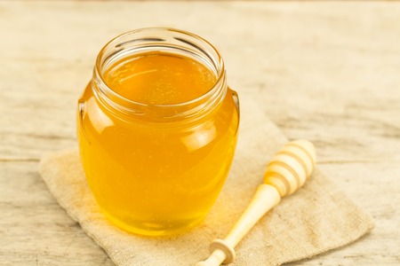 glass jar of honey on jute fabric with drizzler on wooden backgroundの写真素材