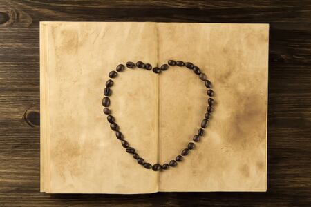 roasted coffee beans in shape of heart on old vintage open bookの写真素材